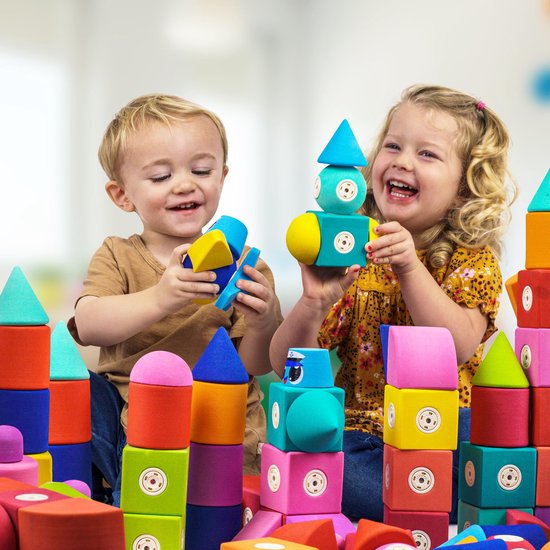 Twee lachende kinderen spelen met kleurrijke magnetische bouwblokken in zachte, ronde vormen.
