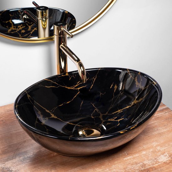 Lavabo noir avec imprimé marbre et veines dorées, robinetterie dorée. Posé sur un plateau en bois.