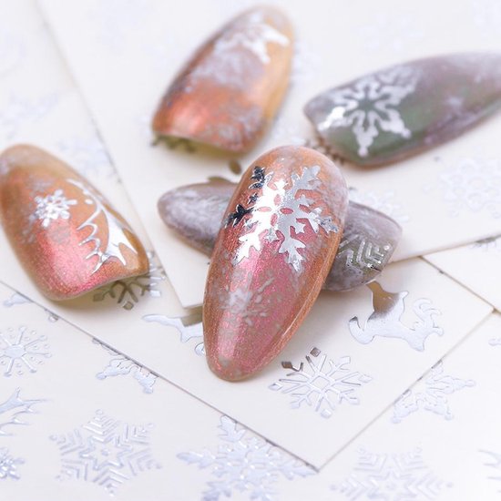 Kunstnagels met zilveren winterse versieringen, zoals sneeuwvlokken en kerstbomen, op een glanzende roze en groene ondergrond.