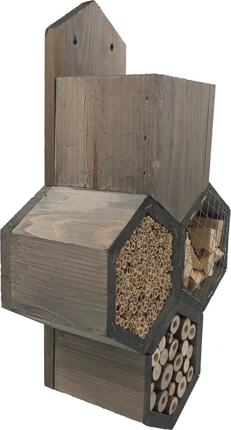 Een grijs houten insectenhotel met compartimenten gevuld met riet, houtblokjes en houtsnippers.