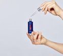 Handen houden een flesje L'Oréal Paris Revitalift Laser Puur Retinol Nacht Serum onder een druppel.