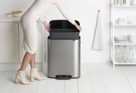Vrouw met witte jurk en laarsjes plaatst binnenemmer in rvs Brabantia pedaalemmer.