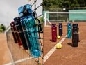 Meerdere King Mungo drinkflessen op een tennisnet en op een tennisbaan.