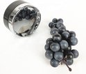 Zwarte draaiasbak met yin-yang motief en chroomkleurige rand, naast een tros donkerblauwe druiven.
