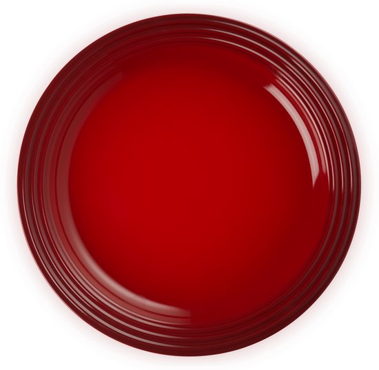 Rond kersenrood dinerbord met gegroefde randen, bovenaanzicht op zwarte achtergrond.