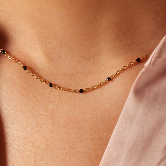 Gouden ketting met kleine zwarte kraaltjes op de huid gedragen.