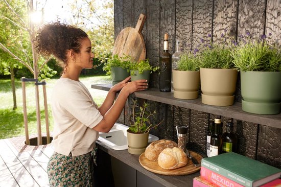 Vrouw rangschikt zandkleurige en groene bloempotten met planten op een houten plank.