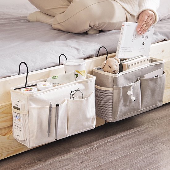 Twee stoffen bedorganizers, een witte en een grijze, hangend aan een houten bedrand. De witte organizer bevat pennen, een bril en een afstandsbediening.