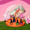 Vier SHATY BIAB nagellak flessen (oranje, blauw, groen, fuchsia) op een oranje plateau omringd door bloemen en gras.
