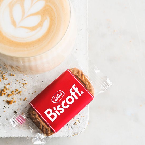 Lotus Biscoff speculaasje in rode verpakking naast een kopje koffie met melkschuim.