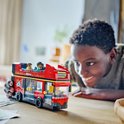 Jongen kijkt naar een rode LEGO dubbeldekker bus met passagiers op het bovendek.