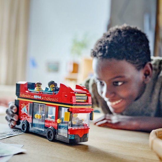 Jongen kijkt naar een rode LEGO dubbeldekker bus met passagiers op het bovendek.