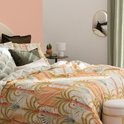 Gouden spiegel in organische vorm, reflecteert een slaapkamer met een gestreept bed.
