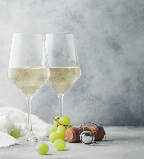Deux verres de vin blanc pétillant, à côté d'une grappe de raisin vert et d'un bouchon de champagne.