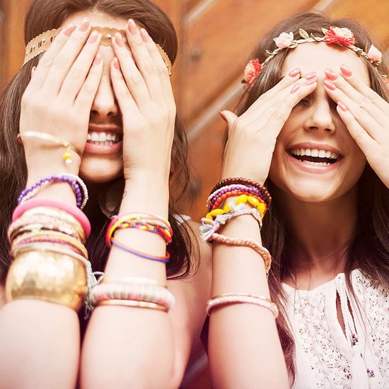 Twee vrouwen bedekken hun ogen met hun handen, lachend en met veel gekleurde armbanden.