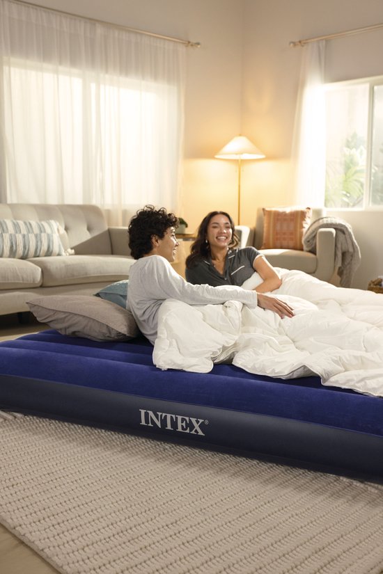 Een koppel ligt op een donkerblauw Intex luchtbed met witte dekens en kussens.