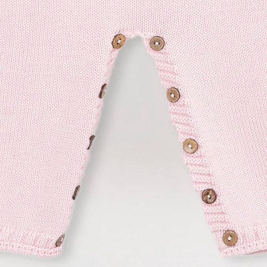 Detail van de onderkant van een gebreide roze romper met houten knoopjes.
