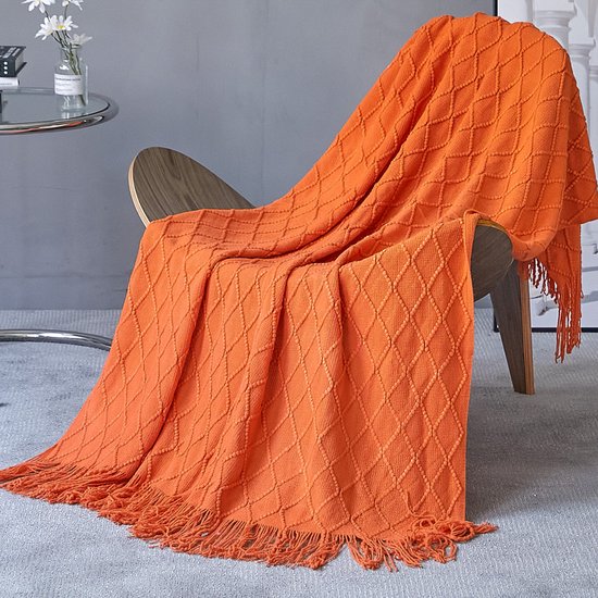 Oranje gebreide deken met ruitpatroon en franjes, gedrapeerd over een houten stoel in een woonkamer.