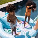 Kinderen spelen in een opblaasbaar zwembad met glijbaan en sproeier. Ze spatten met water en gooien ringen.