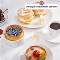 Twee gebakjes met room, een taartje met blauwe bessen, een fruittaartje en een kopje koffie op een marmeren ondergrond.
