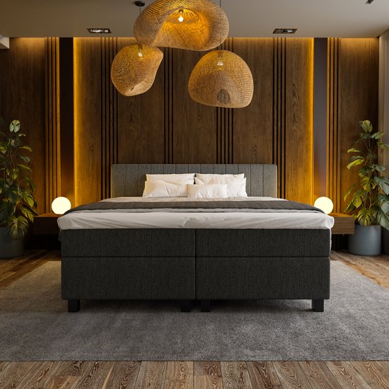 Grijze boxspring bed opgemaakt met witte lakens en grijze deken, in een slaapkamer met houten lamellenwand.