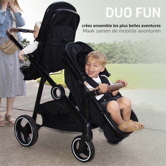 Zwarte tweeling kinderwagen met twee zittende kinderen, een jongen vooraan en een baby achteraan.