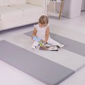 Baby in wit kleding, zittend op een grijze en witte gestreepte speelmat.