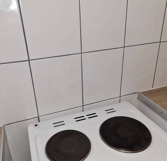 Witte keuken- en wandtegels met grijze voegen boven een fornuis.