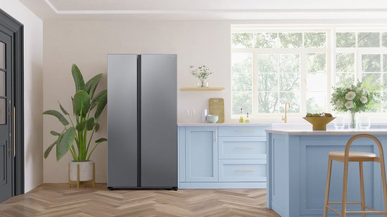 Zilverkleurige Samsung Amerikaanse koelkast in een moderne keuken met blauwe keukenkastjes, een aanrecht en planten.
