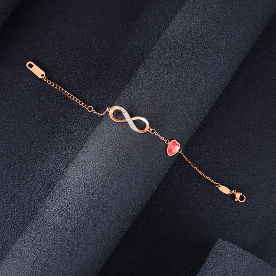 Rosegouden armband met oneindigheidssymbool bezet met zirkonia en een rood hartje, op zwarte achtergrond.