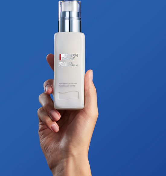 Een hand houdt een witte fles met zilveren pompdispenser vast. "BIOTHERM HOMME BASICS LINE COMFORT BALM" tekst.