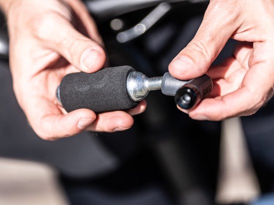 Handen houden een zilveren CO2-patroon met zwarte schuimhoes en adapter vast.