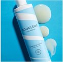 Fles hydraterende haarreiniger met blauwe en witte strepen, met drie druppels product ernaast op een blauwe achtergrond.
