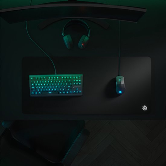 Zwart XXL gaming muismat met SteelSeries logo, met daarop een muis en toetsenbord met blauwe en groene RGB-verlichting. Een koptelefoon hangt boven de monitor.
