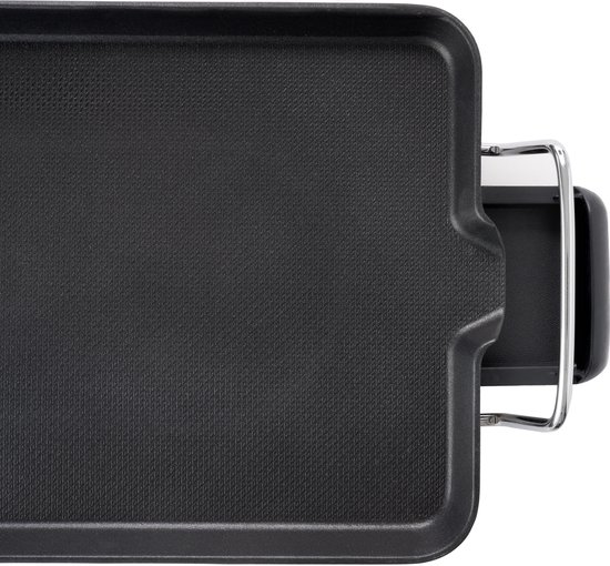 Close-up van een zwart grilloppervlak met een geribbeld gedeelte en een metalen handvat. Een deel van het chromen frame en zwarte voetjes zijn zichtbaar.