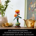 Affichage de chrysanthème LEGO dans un pot vert pastel sur un socle en bois, avec une toile et des vases.