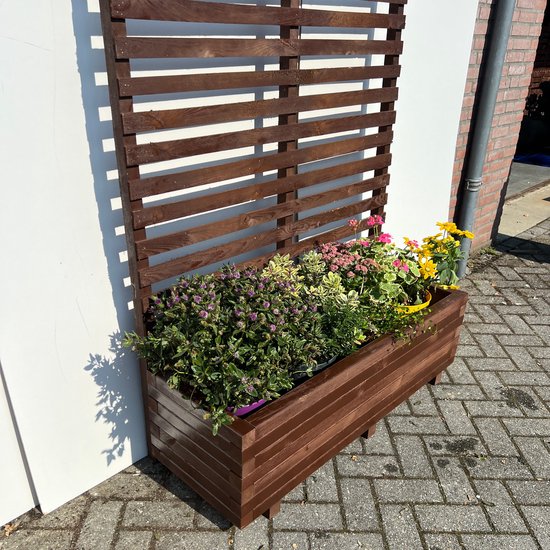 Bruine houten plantenbak met klimrek, gevuld met paarse en roze bloemen en groene planten.