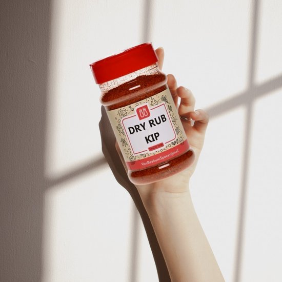 Hand die een "DRY RUB KIP Sinds 1908" strooibus vasthoudt. Rode dop, specerijen zichtbaar, schaduwen.