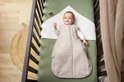 Baby in een lichtgrijze Meyco slaapzak liggend in een wieg, blij kijkend naar de camera.
