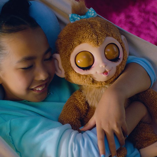 Een meisje knuffelt met een bruine pluche aap met grote ogen, een blauwe strik op zijn hoofd en een roze mond.