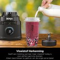 Een hand wordt bijgevuld met melk in een smoothiebeker met bessen en een blenderbasis. Een extra mes is zichtbaar.