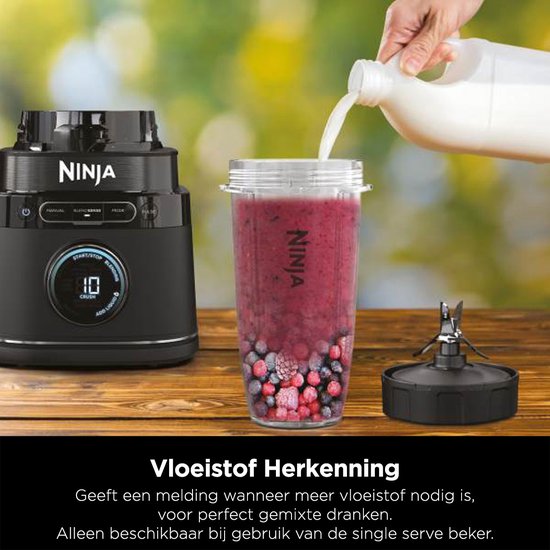 Een hand wordt bijgevuld met melk in een smoothiebeker met bessen en een blenderbasis. Een extra mes is zichtbaar.