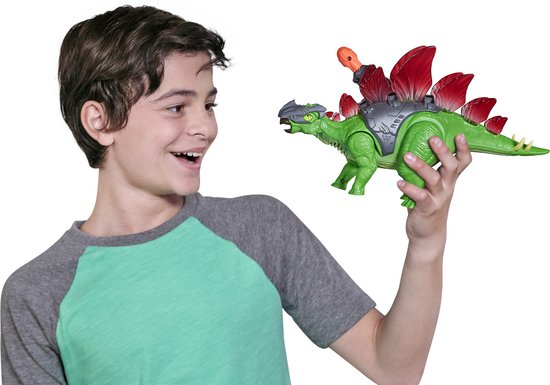 Jongen met een grijze T-shirt houdt een groene Stegosaurus speelgoed dinosaurus met rode rugplaten vast.
