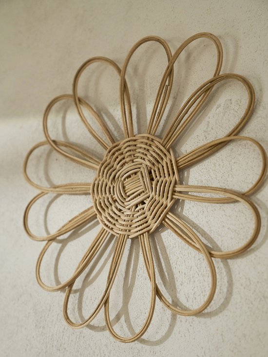 Une décoration murale en rotin en forme de fleur, avec un centre tressé et dix pétales ouverts, sur un mur.