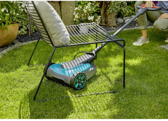 Grastrimmer op het gras onder een metalen rek. Een vrouw is op de achtergrond.