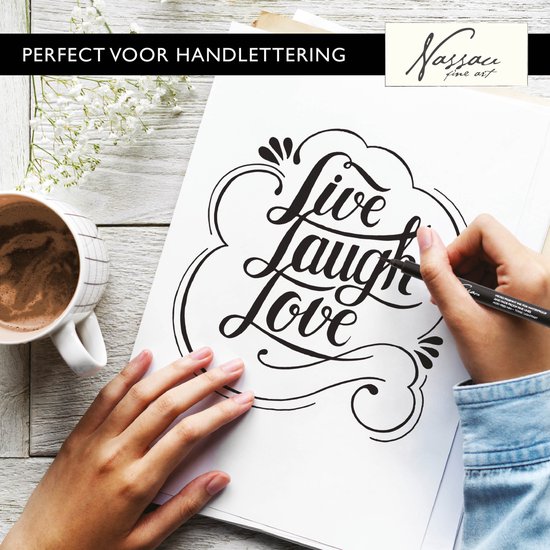 Une main utilise un fineliner noir Nassau Fine Art pour écrire 'Live Laugh Love', à côté d'une tasse de café.