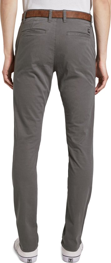 Achterkant van een man in een grijze chino met bruine riem en witte sneakers.