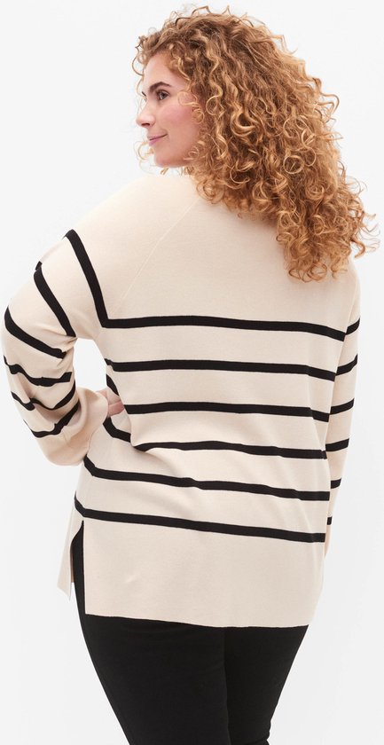 Model met blonde krullen draagt een gebreide trui met horizontale zwart-witte strepen en splitten aan de zijkant.