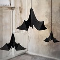 Drie zwarte papieren vleermuizen van verschillende groottes hangen in een kamer met een oud raam en radiator.