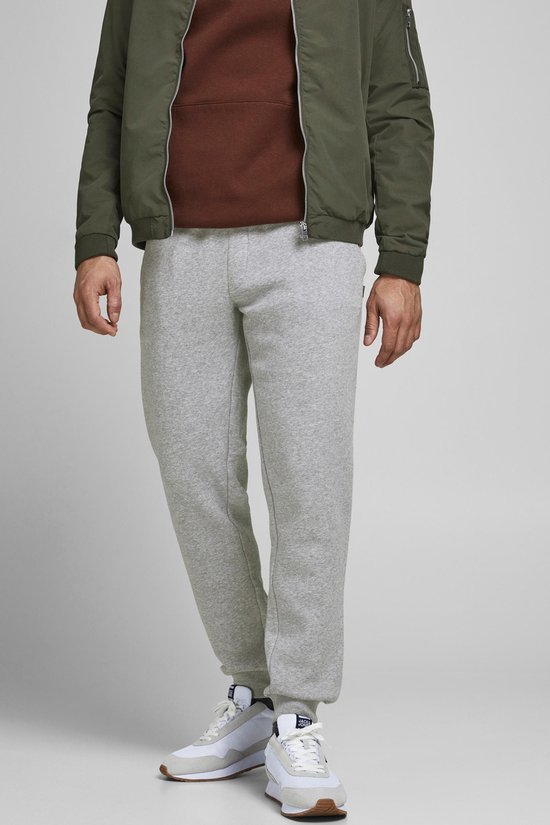 Close-up van een man in een lichtgrijze joggingbroek, groene bomberjack en bruine hoodie.